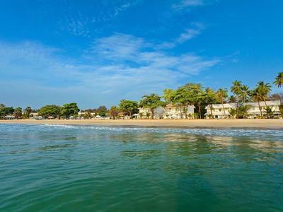 Strand mit weißen Sand, Palmen und Häusern unter blauem Himmel und ruhigem Meerwasser.