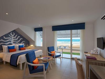 Helles Hotelzimmer mit Meerblick, Doppelbett, blauen Akzenten und Balkon mit Sitzbereich.
