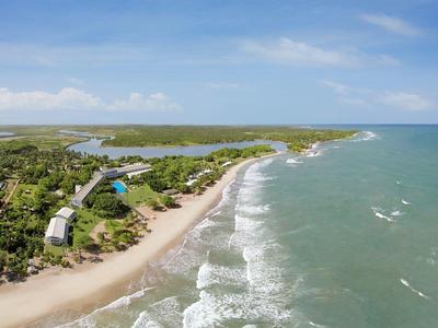 Küste mit Sandstrand, Wellen und grünen Bäumen entlang des blauen Ozeans bei klarem Himmel.