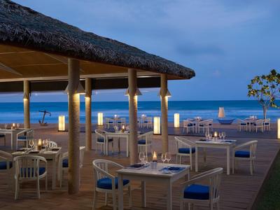 Außenrestaurant mit weißen Tischen und Stühlen, Blick auf Meer und blauen Himmel bei Abenddämmerung.