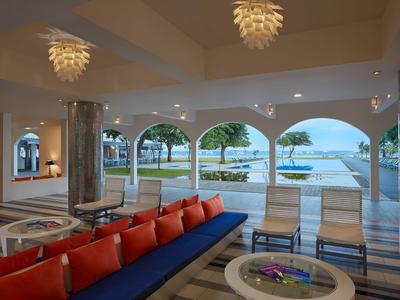 Accogliente area lounge dell'hotel con divano rosso, sedie e vista sulla piscina e sul giardino.