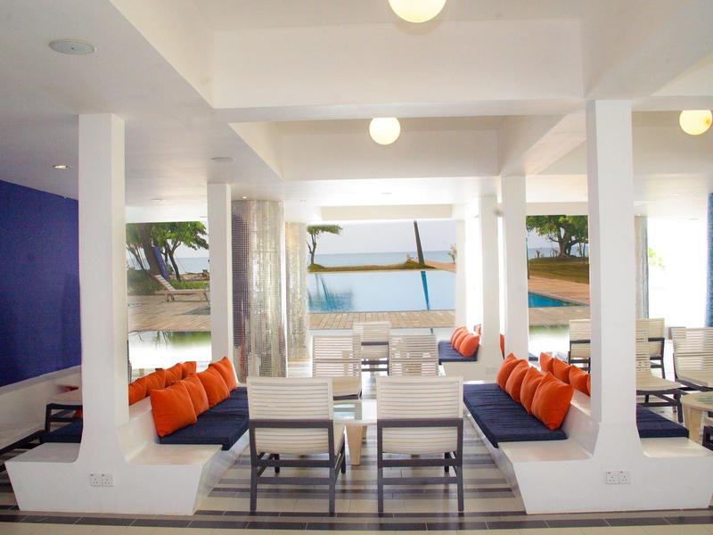 Moderner, heller Lounge-Bereich mit weißen Möbeln, blauer Wand und orangefarbenen Kissen am Meer.