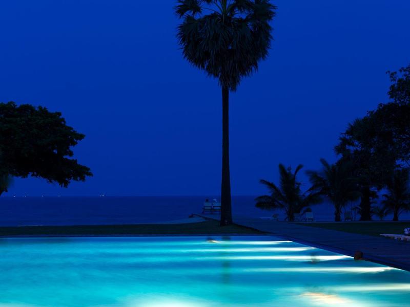 Beleuchteter Pool bei Nacht mit Palmen und dunklem Himmel im Hintergrund.