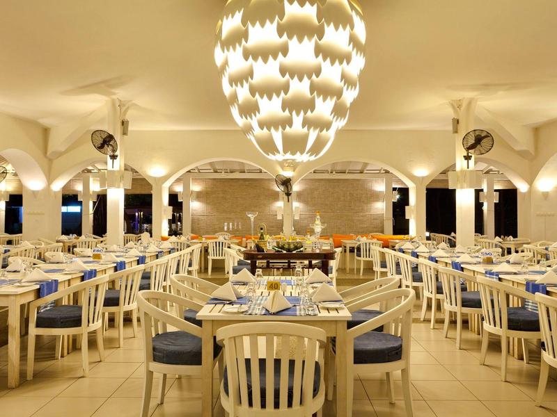 Großer, heller Speisesaal mit weißen Holzstühlen, blauen Polstern und stilvollen Kronleuchtern.