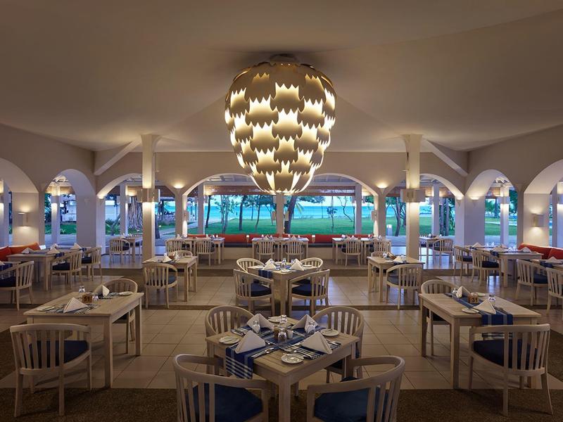 Großes Restaurant mit weißem Mobiliar, blauen Sitzpolstern, runden Tischen und auffälliger Deckenleuchte.