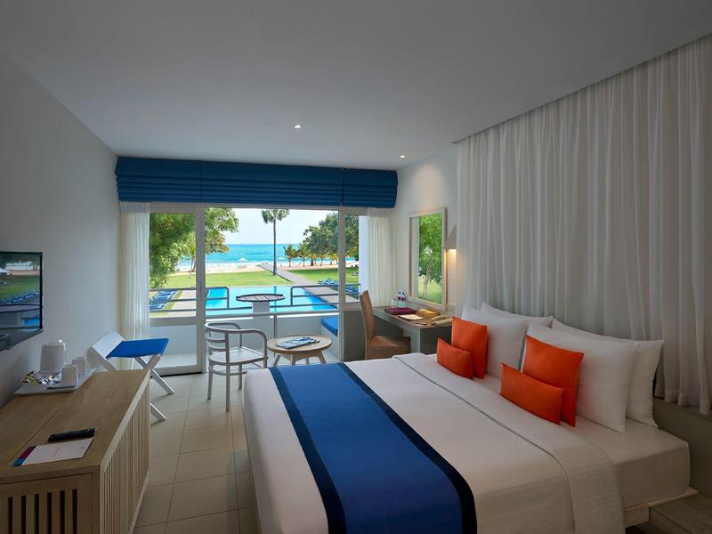 Modernes Hotelzimmer mit Doppelbett, blauen Akzenten, Terrasse und Blick auf Pool und Meer.