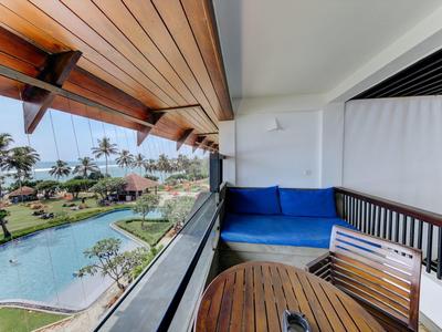 Balkon mit blauem Sofa, Holztisch und Stühlen, Blick auf Pool und Palmen unter blauem Himmel.