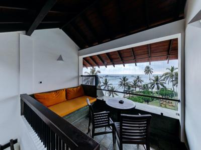 Balkon mit Holzdach, gelbem Ecksofa, schwarzem Tisch und zwei Stühlen, Palmen im Hintergrund.