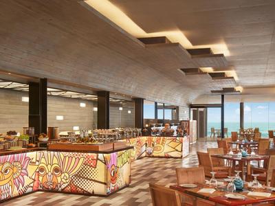 Ein modernes Restaurant mit Holztischen, braunen Sesseln und buntem, beleuchtetem Buffet.