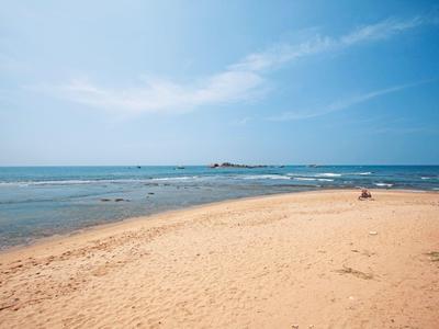 Weiter Sandstrand mit ruhigem Meer, blauem Himmel und wenigen Wolken am Horizont.
