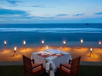 Romantisches Abendessen mit Tisch am Strand und Blick auf das Meer bei Sonnenuntergang.