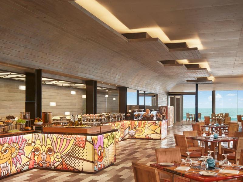 Ein modernes Restaurant mit Holztischen, braunen Sesseln und buntem, beleuchtetem Buffet.