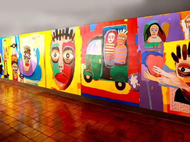 Lange Wand mit bunten, großen Gemälden, die verschiedene Gesichter und Figuren zeigen.