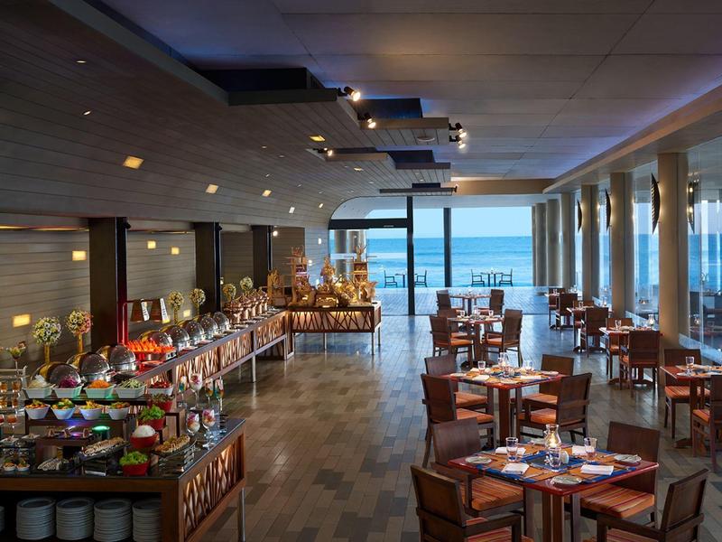 Großzügiges Restaurant mit Holzboden, Holztischen, Stuhlgruppen und großer Fensterfront mit Meerblick.