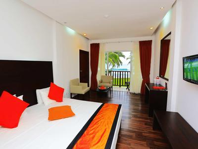 Habitación de hotel moderna con cama doble, almohadas coloridas y balcón con vistas a palmeras.