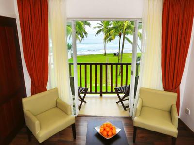 Habitación de hotel con dos sillones y balcón con vista a palmeras y mar.