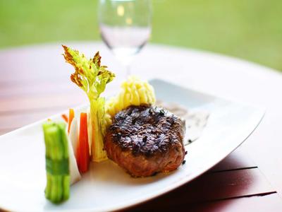 Bistec a la parrilla con verduras en plato blanco servido sobre mesa de madera.