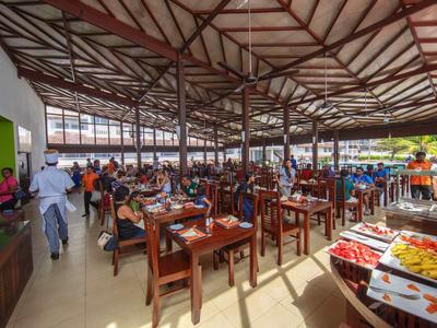 Área de comedor abierta con sillas de madera, mesas y buffet en un hotel con vista al exterior.