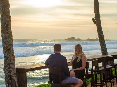 Dos personas sentadas en un bar de la playa con vista al mar al atardecer.