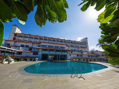 Hotel con piscina redonda y sombrillas, enmarcado por hojas verdes.