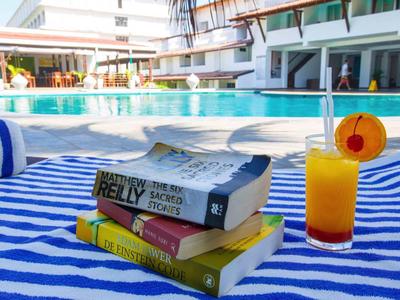Una pila de libros y una bebida junto a una piscina en una silla azul.