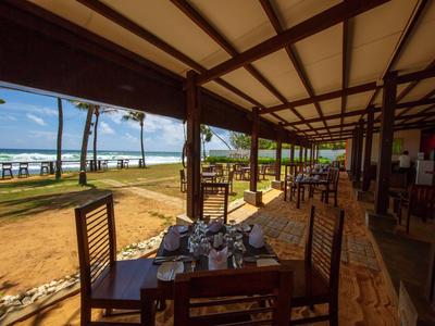 Área de comedor abierta de hotel con mesas de madera y vistas a palmeras y mar.