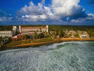 Edificio de hotel en una costa boscosa con mar agitado bajo un cielo nublado.
