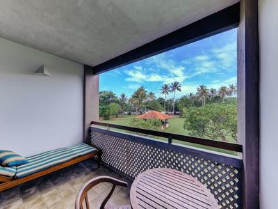 Balkon z krzesłem, leżanką i widokiem na ogród z palmami i czystym niebem.