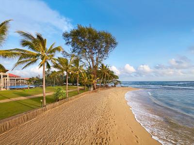 Plaża z złotym piaskiem, palmami i jasnym błękitnym niebem przy ośrodku