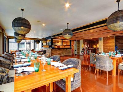 Nowoczesna restauracja z drewnianymi stołami, wiklinowymi krzesłami i dużymi wiszącymi lampami w ciepłej atmosferze.