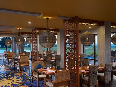 Restauracja z drewnianymi meblami i dużymi okrągłymi lampami z widokiem na morze.