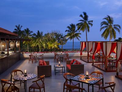 Área exterior abierta con mesas iluminadas y palmeras al anochecer junto al mar.