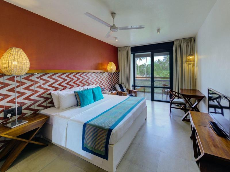 Nowoczesny pokój hotelowy z dużym łóżkiem, kolorowymi akcentami i widokiem na balkon.