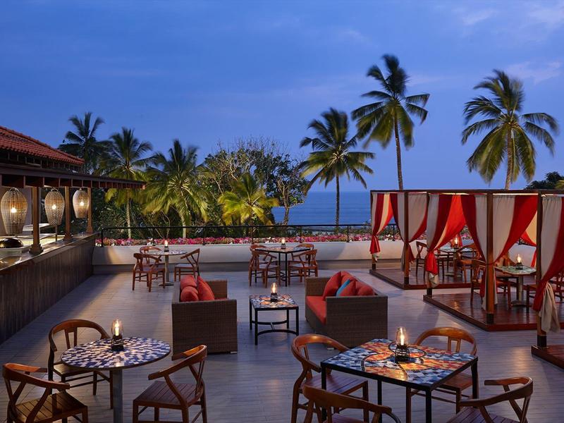 Wieczorny taras z miejscami do siedzenia, światłem świec i palmami przy morzu.