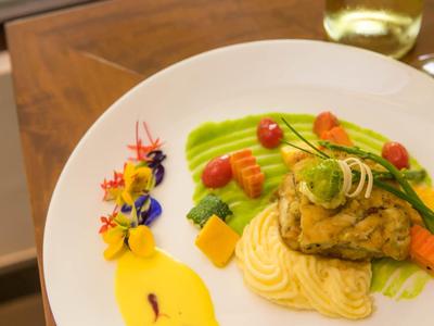 Kunstig opgemaakt visgerecht met groenten en saus op wit bord.