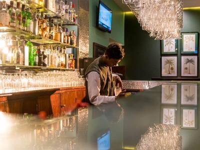 Person sitzt alleine an einer Bar mit Glasregalen und Fernseher im Hintergrund.