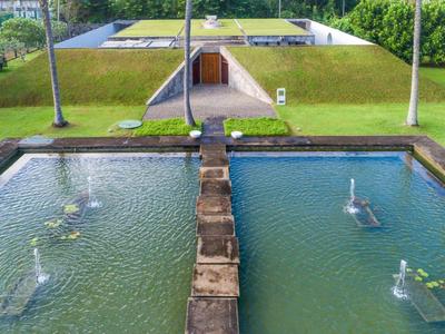 Een rechthoekige waterfontein met vijf sproeiers voor een geplaveid pad en groen gras.