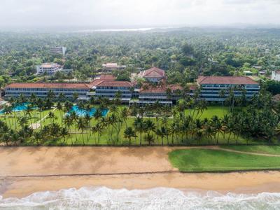 Luchtfoto van een resort met meerdere gebouwen, een groot zwembad en directe toegang tot het strand.