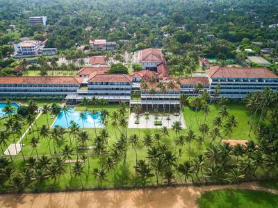 Luchtfoto van een resort aan het strand met zwembaden en palmbomen.