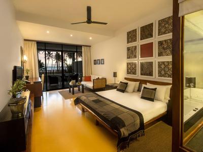 Moderne hotelkamer met tweepersoonsbed, balkonuitzicht en zee bij zonsondergang.