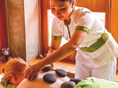 Een masseuse legt hete stenen op de rug van een liggende vrouw in een spa-ruimte.