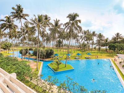 Großer blauer Pool mit Palmen und grünen Inseln in tropischem Hotelresort.