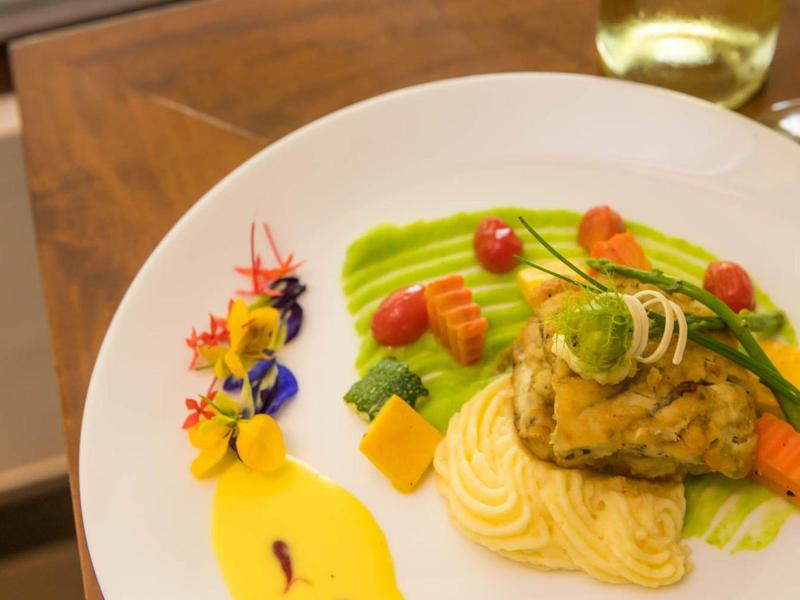 Kunstig opgemaakt visgerecht met groenten en saus op wit bord.