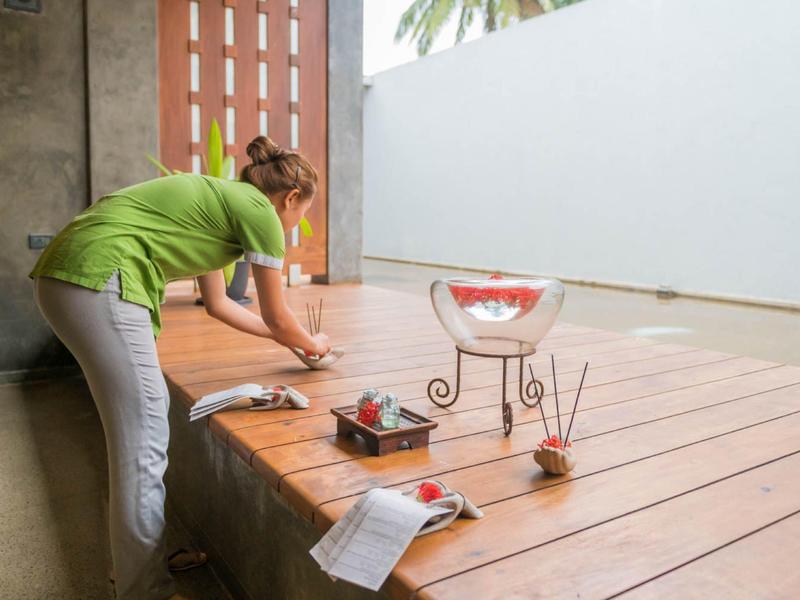 Vrouw in groen shirt dekt een tafel op een houten terras met uitzicht op zee.