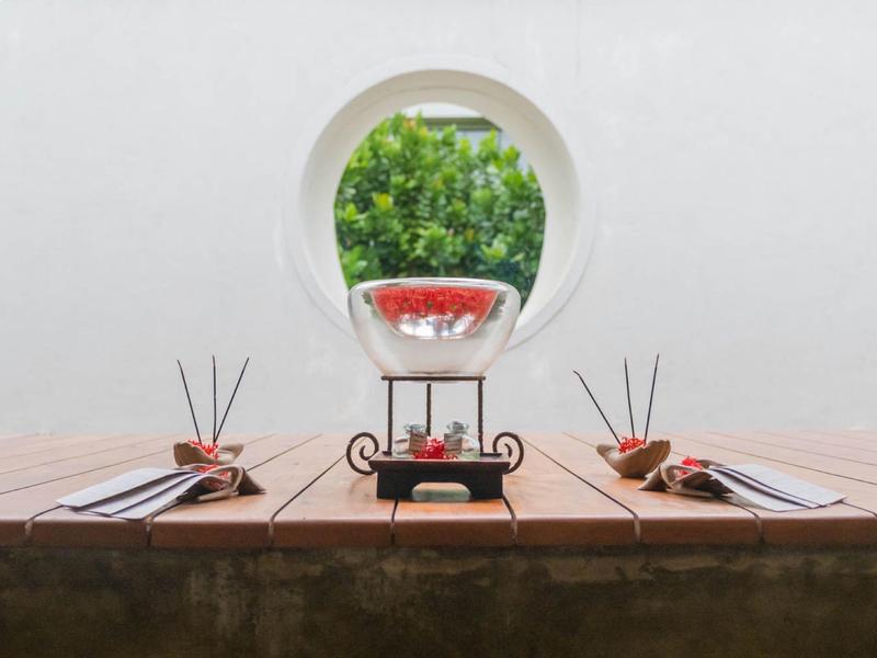 Twee gedekte houten tafels met een decoratieve karaf en uitzicht op een boom door een rond raam.