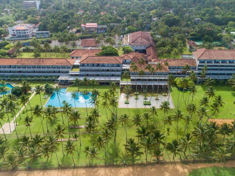 Groot hotel met zwembaden, palmbomen en uitgestrekte groene gebieden in een tropische omgeving.