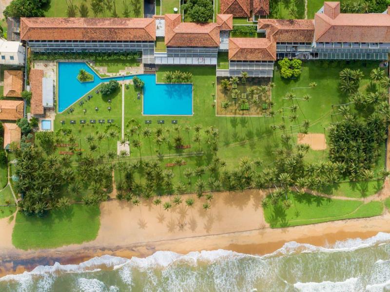 Luchtfoto van een hotel met zwembad, tuin en strand aan zee.