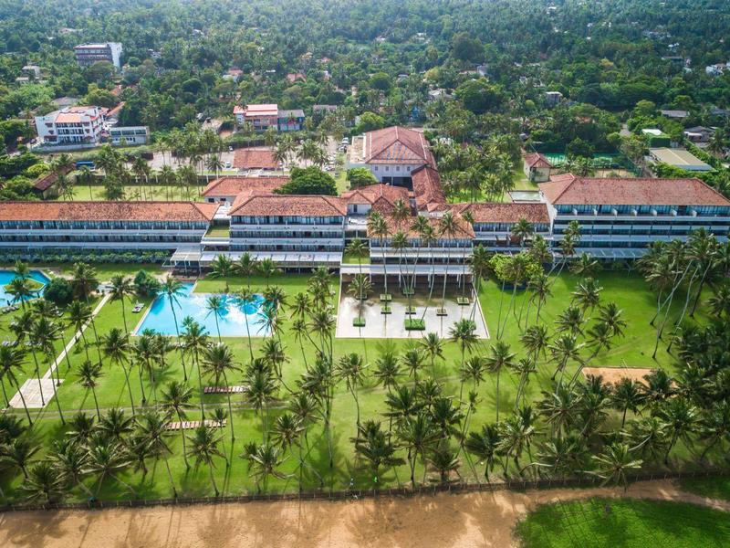 Luchtfoto van een resort aan het strand met zwembaden en palmbomen.