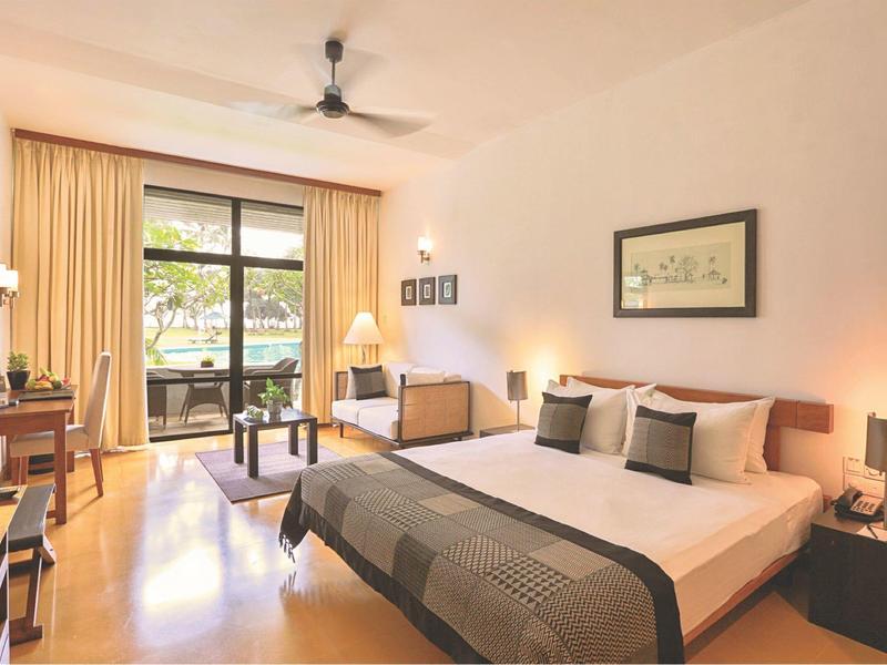 Modern hotelkamer met groot bed, balkon en plafondventilator.