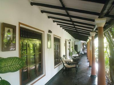 Überdachte Veranda mit Stühlen an einem Gebäude, umgeben von Bäumen und natürlichem Licht.